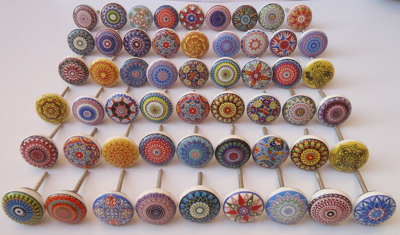 May include: A collection of 40 colourful ceramic cabinet knobs with intricate mandala designs. The knobs are white with a variety of colours, including red, blue, yellow, green, and orange. Each knob has a silver screw.