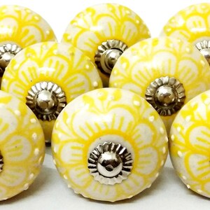Peut inclure: Ensemble de dix boutons de meuble en c&eacute;ramique jaune et blanc. Chaque bouton pr&eacute;sente un motif floral et une base en m&eacute;tal argent&eacute;. Ces boutons d&eacute;coratifs mesurent environ 4 cm de diam&egrave;tre.