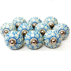 May include: A set of ceramic cabinet knobs featuring a floral design. The knobs are predominantly white with blue floral patterns and silver-coloured metal hardware. The knobs are round and decorative.