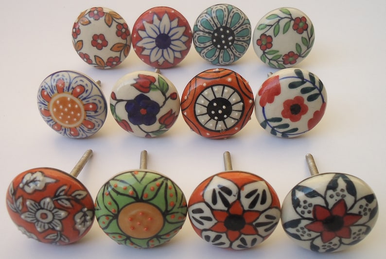 Pode incluir: Doze bot&otilde;es de cer&acirc;mica com desenhos florais e geom&eacute;tricos em tons de laranja, azul, verde, branco e preto. Os bot&otilde;es t&ecirc;m parafusos prateados.