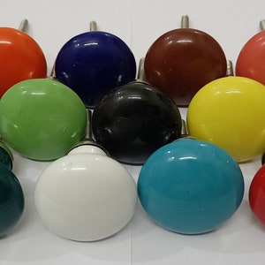 Könnte beinhalten: Sortiment von 12 Keramik-Schrankknöpfen in verschiedenen Farben, darunter Rot, Orange, Gelb, Grün, Blau, Türkis, Grau, Weiß, Schwarz, Braun und Rosa.