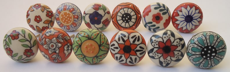 Pode incluir: Doze bot&otilde;es de gaveta de cer&acirc;mica com v&aacute;rios padr&otilde;es florais e geom&eacute;tricos em tons de branco, vermelho, laranja, verde, azul e preto.