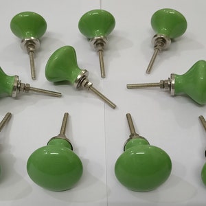 May include: Ten green ceramic cabinet knobs with silver metal screws. The knobs have a rounded, slightly oval shape.