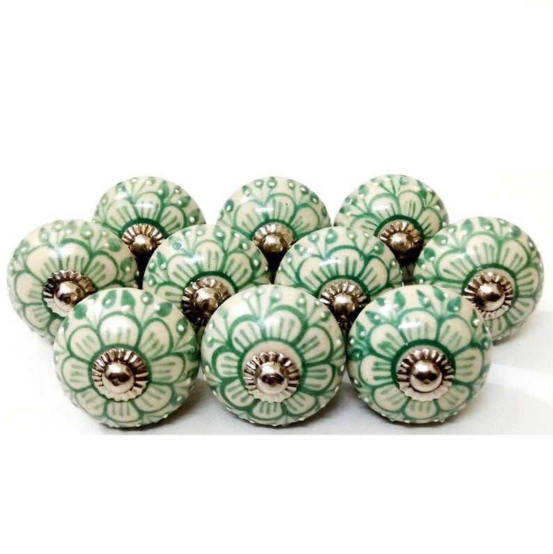 Peut inclure: Dix boutons de meuble en c&eacute;ramique, cr&egrave;me et vert. Chaque bouton pr&eacute;sente un motif floral vert sur un fond cr&egrave;me. Les boutons ont des fixations m&eacute;talliques argent&eacute;es.