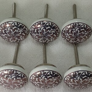 K&ouml;nnte beinhalten: Zehn wei&szlig;e Keramik-Schrankkn&ouml;pfe mit einer silbernen Schraube. Jeder Knopf hat ein braunes und wei&szlig;es Blumenmuster.