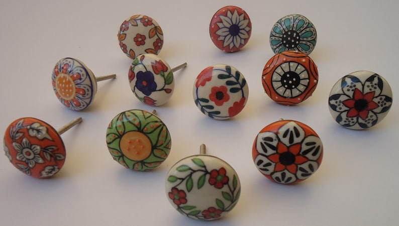Pode incluir: Doze bot&otilde;es de gaveta de cer&acirc;mica com desenhos florais e geom&eacute;tricos coloridos. Os bot&otilde;es s&atilde;o redondos e t&ecirc;m um parafuso prateado.