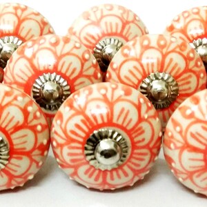 Peut inclure: Ensemble de dix boutons de meubles en c&eacute;ramique. Chaque bouton pr&eacute;sente une base cr&egrave;me avec un motif floral corail. Les boutons ont une base en m&eacute;tal argent&eacute;. Id&eacute;al pour ajouter une touche d&eacute;corative aux meubles.