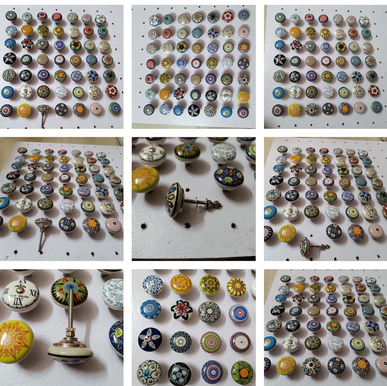 May include: A collection of colorful ceramic cabinet knobs with various floral and geometric designs. The knobs feature a range of colors, including blue, yellow, green, and red, and are mounted on a white surface. Some knobs have a silver metal base.