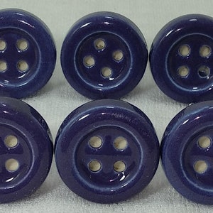 Op de afbeelding: Tien keramische knoppen in een diepe paarse kleur met een wit knoopontwerp. Elke knop heeft vier gaten in de knop.
