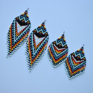 May include: A pair of beaded earrings with a geometric pattern in shades of blue, orange, yellow, white, and black. The earrings are teardrop shaped and have a fringe.