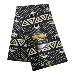 May include: Folded black fabric featuring a geometric pattern of white lines, triangles, and circles, with yellow dot accents. The fabric has a tag with text. The design is striking and graphic.