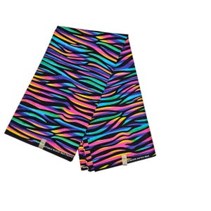 May include: A folded piece of fabric with a vibrant zebra stripe pattern in shades of pink, yellow, blue, and green on a black background. The fabric has tags that read "SUITABLE BLOCK WAX PRINTS" and "PRINCESS DUTCH WAX".