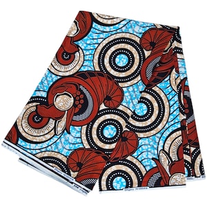 May include: Folded fabric with a vibrant African wax print. The design features large, stylized brown and cream-coloured shapes against a light blue background, with black and white circular patterns. The fabric is folded and stacked.