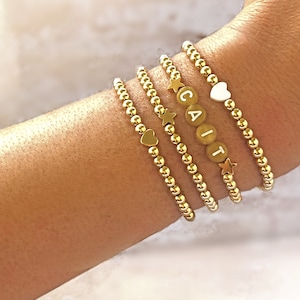 May include: Four gold beaded bracelets with small charms. The charms include a heart, a star, and the letters "GAIT".