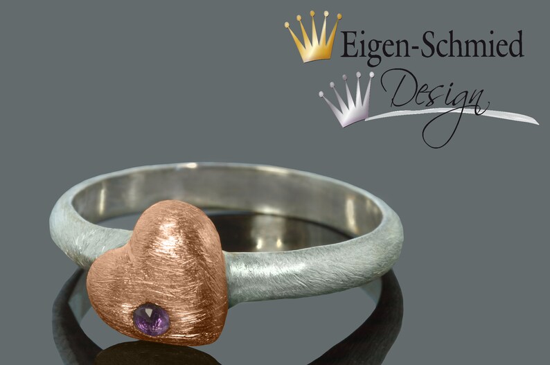 Puede incluir: Un anillo de plata con un engaste en forma de coraz&oacute;n de oro rosa con una peque&ntilde;a piedra preciosa p&uacute;rpura. El anillo est&aacute; hecho por Eigen-Schmied Design.