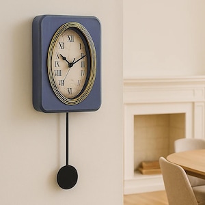 May include: A blue wall clock with a gold-trimmed oval clock face and black Roman numerals. The clock has a black pendulum and is mounted on a white wall. The clock is a decorative item.