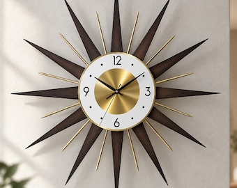 May include: A starburst wall clock featuring a central circular face with a brushed gold center, a white outer ring, and black numerals at the 3, 6, 9, and 12 positions. The clock has long, pointed dark wood rays and thinner gold metal spokes.