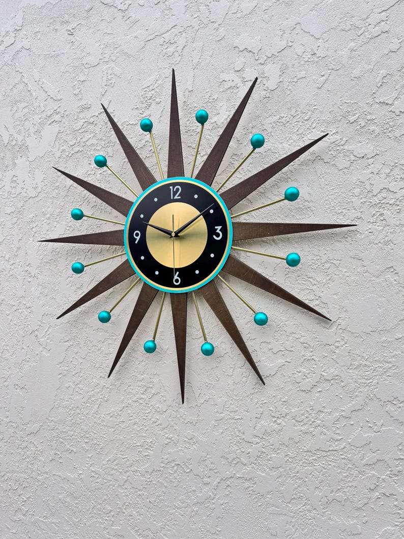 May include: A large, starburst-shaped clock with a black face and gold accents. The clock has turquoise blue accents on the tips of the starburst and around the face. The clock face has black Roman numeral hour markers and gold hands.