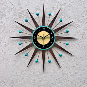 May include: A mid-century modern style wall clock with a black face, gold hands, and turquoise accents. The clock has a starburst design with 12 points.
