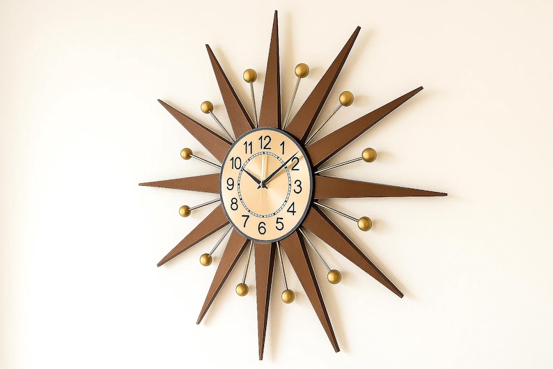 May include: A starburst-shaped wall clock with a light wood-tone face and black hands. The clock features brown wooden rays with gold-colored ball accents. The clock's numbers are black, and the frame is black.