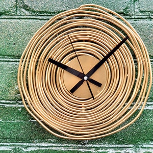 May include: A gold-colored clock with a circular face and black hands. The clock face is made of concentric circles of metal wire.