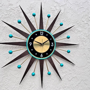 May include: A mid-century modern style wall clock with a black face and gold hands. The clock has a turquoise rim and 12 gold-tipped rays with turquoise balls at the ends.