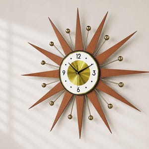 May include: A mid-century modern starburst wall clock. The clock features a brown wooden starburst design with gold-colored accents and a white clock face with black numerals. The clock hands are black.