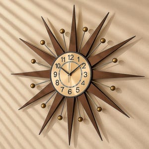 May include: A starburst wall clock with a gold-tone face and black numerals. The clock has brown, pointed rays extending outward, with small gold-colored spheres at the tips. The clock is mounted on a beige wall.