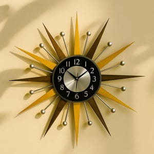 Może przedstawiać: Zegar ścienny w stylu retro z motywem rozbłysku gwiazdy. Zegar ma czarną tarczę ze srebrnymi wskazówkami i cyframi. Rozbłysk gwiazdy ma naprzemienne brązowe i żółto-złote drewniane kolce ze srebrnymi kulkowymi akcentami.