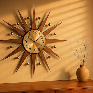 May include: A starburst-shaped wall clock with a gold face and black numerals. The clock has brown wooden rays and gold accents. A vase with branches sits on a wooden cabinet, with a window and blinds in the background.