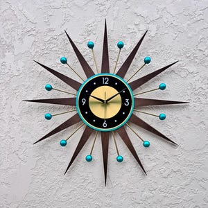 May include: A brown and gold starburst clock with turquoise accents. The clock face is black with gold numbers and hands.