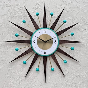May include: A mid-century modern starburst clock with teal accents. The clock face is white with black numbers and gold hands. The clock has a gold center and a teal outer ring.