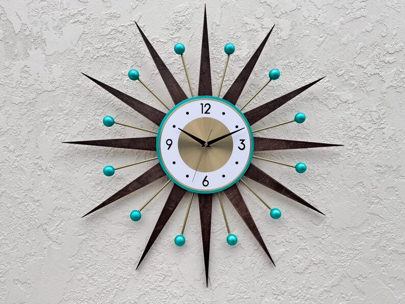May include: A mid-century modern starburst clock with teal accents. The clock face is white with black numbers and gold hands. The clock has a gold center and a teal outer ring.