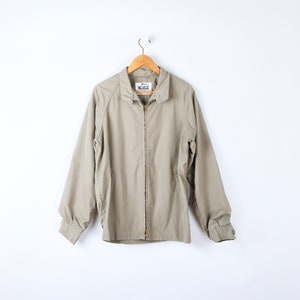 May include: A beige zip-up jacket with a  "The Original  Wrangler" label hanging on a wooden hanger.