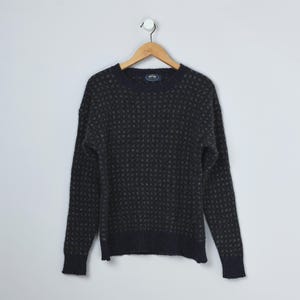 May include: A dark navy blue sweater with a textured pattern, hanging on a wooden hanger against a white background. The sweater has long sleeves and a crew neck. The pattern is a repeating dot design in a lighter shade of blue.