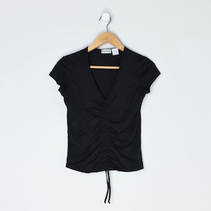 May include: Black short-sleeve top with a V-neck and gathered front detail. The shirt hangs on a wooden hanger against a white background. A drawstring is visible at the bottom of the shirt.