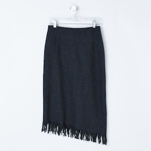 May include: A dark gray pencil skirt with a fringed hem, hanging on a white background. The skirt is made of a textured fabric and has a straight silhouette. The fringe adds a decorative element to the bottom.