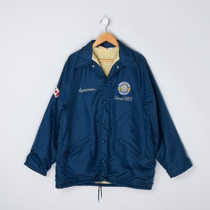May include: A blue workwear jacket with a fleece lining. The jacket has a snap closure and two pockets. It features an embroidered logo with the text "Local 920" and the words "spaceman" on the left side.