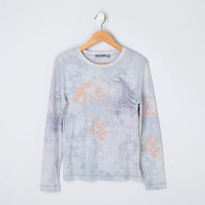 May include: A light blue long-sleeved shirt with a floral and bird print. The shirt has a crew neck and a relaxed fit.