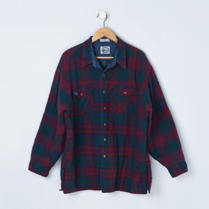 May include: A long-sleeved, button-down flannel shirt in a plaid pattern of burgundy, navy blue, and forest green. The shirt has a denim collar and two chest pockets. It is hanging on a wooden hanger.