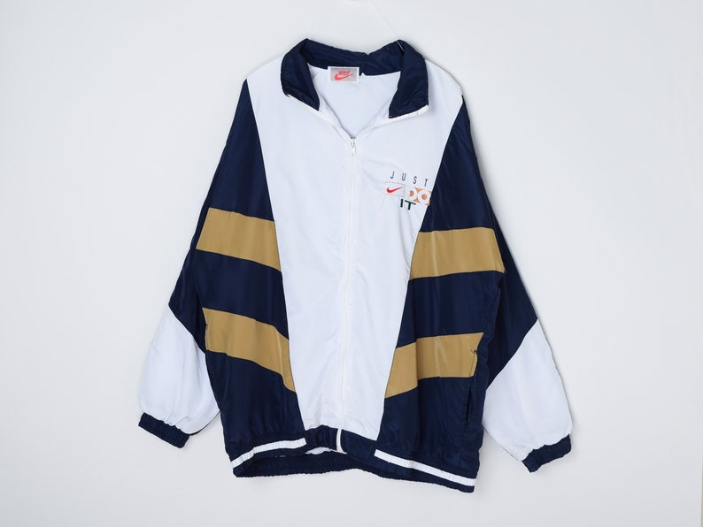 May include: A white, blue, and gold windbreaker jacket with a zipper closure. The jacket has a large "JUST DO IT" logo on the front with a Nike swoosh.