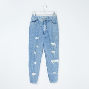 Puede incluir: Vaqueros azul claro con lavado ácido y detalles desgastados. Los pantalones vaqueros de cintura alta tienen múltiples roturas y desgarros en las piernas. Los vaqueros cuelgan de una percha de plástico transparente sobre un fondo blanco.