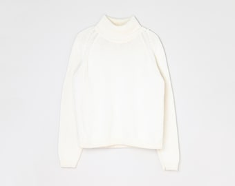 May include: Ivory-colored turtleneck sweater. The long-sleeved sweater has a ribbed hem and cuffs, and a ribbed turtleneck collar. The shoulders have a decorative knit pattern. The sweater is made of a soft, knitted material.