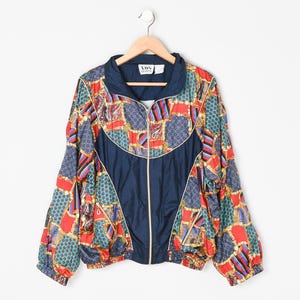 May include: A zip-up windbreaker jacket featuring a vibrant patchwork pattern of red, blue, and gold chain-link motifs. The jacket has solid navy blue panels on the chest and a high collar. A white label with the text VDS SPORTS is at the neck.