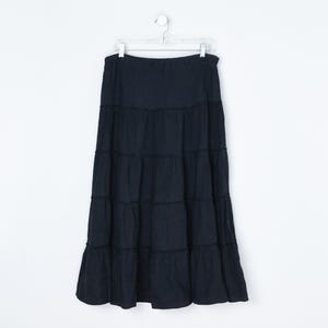 May include: A long, tiered black skirt hanging on a white hanger against a white background. The skirt has a wide waistband and multiple horizontal seams creating a layered effect. The skirt is made of a flowing fabric.