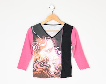 Op de afbeelding: Roze, zwart en wit langarm shirt met een grafische print van een draaiende abstract gezicht.