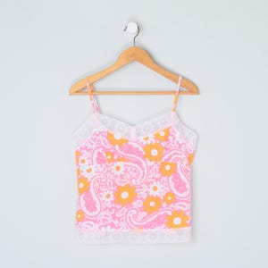 Puede incluir: Un top rosa y naranja sin mangas con un estampado floral paisley y ribete de encaje blanco.