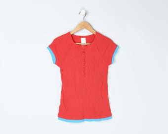 May include: A red short-sleeved shirt with a henley neckline and light blue trim on the sleeves and hem. The shirt is hanging on a wooden hanger against a white background.