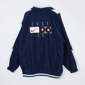 May include: A navy blue windbreaker jacket with white accents on the sleeves and hem. The back of the jacket features a white "JUST DO IT" logo with a Nike swoosh.