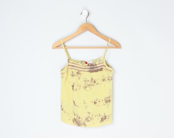 Pode incluir: Top camisola amarelo tie-dye com alças finas, pendurado em um cabide de madeira. O top apresenta detalhes bordados marrons na gola e um padrão tie-dye em tons de marrom e amarelo.